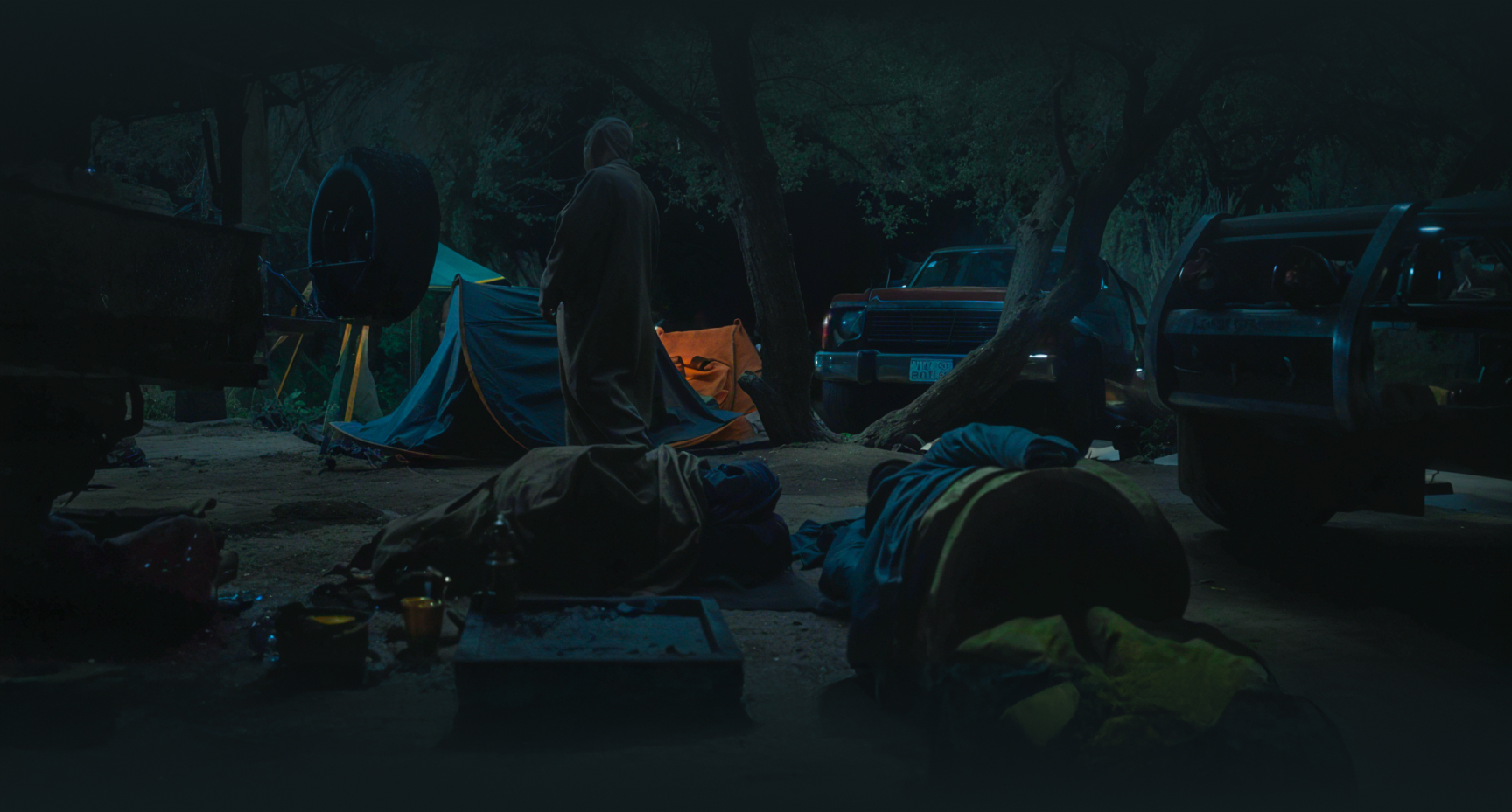 a group of people in a dark area with tents and a car